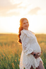 Fototapeta na wymiar Happy pregnant woman walks among meadow at sunset.
