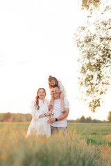 Fototapeta premium Family walks on meadow and father carries daughter on his shoulders.