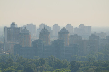Scenic aerial landscape of Kyiv in morning haze. Silhouettes of modern high-rise buildings at smog. Concept of modern architecture from glass, steel and concrete. High-rise houses at smoke