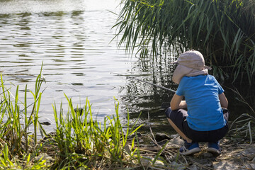 kind angelt alleine am wasser im Mütze und blauem Hemd mit einer rute