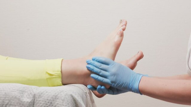 Podologist in blue medical gloves massages a female flat foot. Closeup. Slow motion. Concept of chiropody, podology and spa procedure in beauty salon.