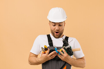 Positive male repairman at home holding various repair tools on beige background