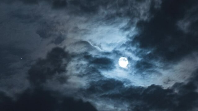 Full moon with moving black clouds. Nighttime timelapse. Clouds floating through the bright disk of the moon. Mysterious night scene