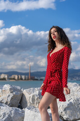 A beautiful portrait of a sexy Caucasian girl with a red dress posing outdoors with blue cloudy sky