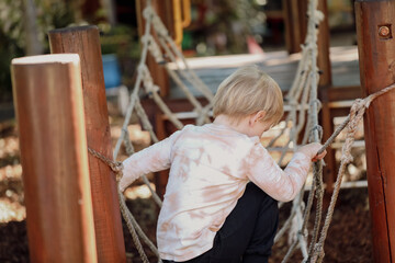 Little preschool girl playing on rope bridge at kindergarten