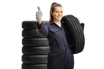Young female mechanic worker carrying a car tire and showing thumbs up