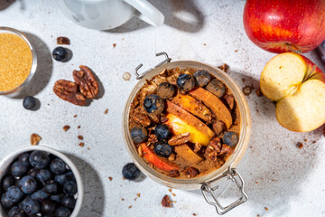 Healthy vegan dietary breakfast or snack. Apple pie overnight oatmeal, oats flakes with apples, yogurt, cinnamon, spices, blueberry. In glass, on a white marble table. Copy space
