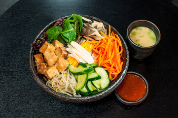Korean Vegetarian Bibimbap, fried tofu bento box hot stone bowl with salads, kimchi, Bibimbap sauce, miso soup on black table background