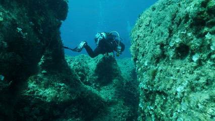 Scuba diver swim through a crack in the rock. Crack in the seabed over tectonic plates. Tiktanic displacement of plates at the bottom of sea. Mediterranean Sea, Cyprus