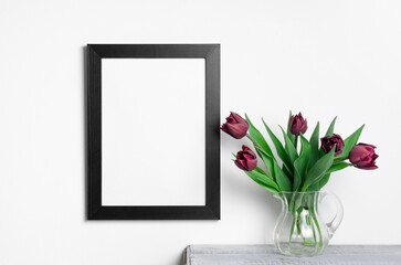 Black frame mockup with tulips flowers bouquet over white wall