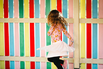 Little girl twirling in front of vibrant rainbow colored wall