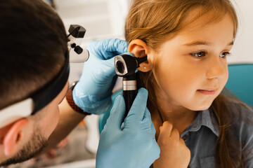ENT doctor otolaryngologist looks through otoscope the ears of a little girl. Otoscopy. Treatment child ear pain.