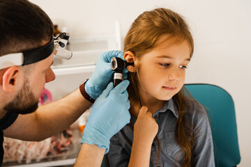 ENT doctor otolaryngologist looks through otoscope the ears of a little girl. Otoscopy. Treatment...