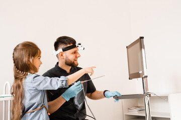 ENT doctor otolaryngologist with headlight showing to child endoscope for rhinoscopy and otoscopy....