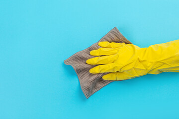 worker hand in a yellow rubber protective glove with a micro fiber cloth wiping a blue wall from dust. A maid or housewife takes care of the house. Spring general or regular cleaning.