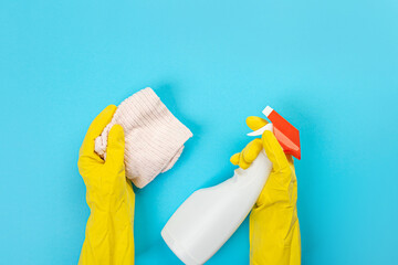 The hands of a housewife in yellow rubber protective gloves hold a bottle of household chemicals and a rag. Detergent for various surfaces in the kitchen, bathroom and other rooms. 