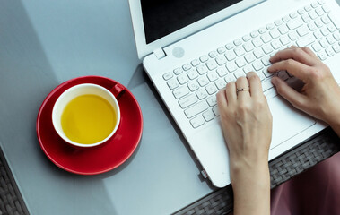 Female hands work on a modern laptop and a cup of