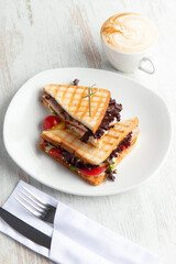 Sandwiches with ham, tomatoes and lettuce in a plate on a wooden table.