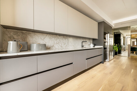 Wall Of A Kitchen With Plain White Base Units And Gray Base Units With White Marble Countertops And Light Brown Wooden Floors