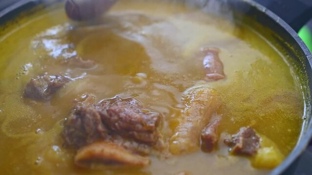 Handheld close up view of wooden ladle showing meat of steaming traditional Dominican creole food called Sancocho