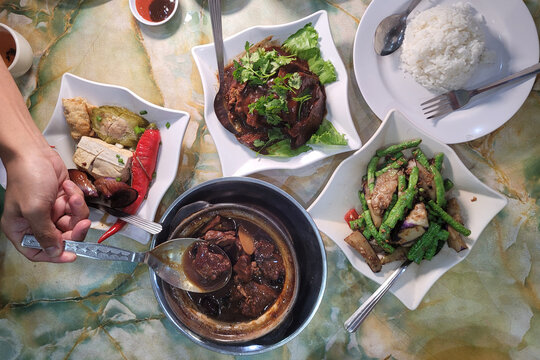 Top view image of traditional Malaysian Chinese food. Stewed lamb in a clay pot, braised pork belly with taro, Hakka Yong Tau Foo, stir fried vegetables served with white rice. 