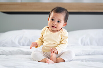 Asian baby girl with white skin and big eyes  naughty age  playing on the bed by the bedroom window