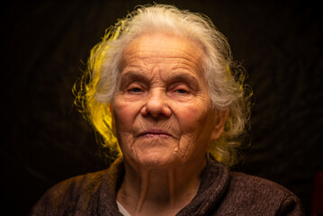 Portrait of beautiful elderly old woman in colorful bright lights blue and yellow, , 70s, grandmother,  on black background., positive, smiling at camera, happy, studio, Close up, gray hair, caucasian