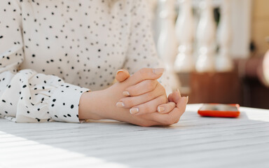 Obraz na płótnie Canvas Close-up of unrecognizable woman waiting with her hands folded together lying on white table of street cafe, outdoors. Selective focus on caucasian female hands with gentle manicure