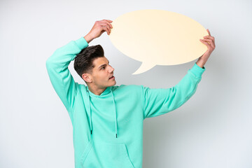 Young handsome caucasian man isolated on white bakcground holding an empty speech bubble and with sad expression