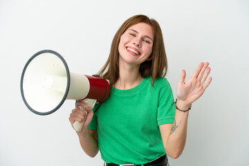 Young English woman isolated on white background holding a megaphone and saluting with hand with happy expression