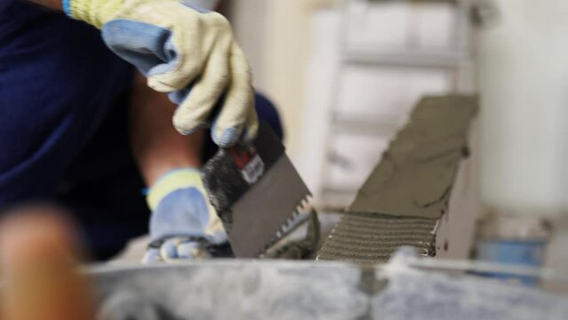Bricklayer applies adhesive glue on autoclaved aerated concrete blocks with notched trowel and spatula. Brickwork worker contractor puts mortar on foam concrete doing masonry on construction site.