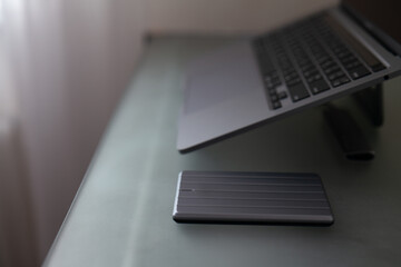 external hard drive in silver color on a computer desk against a blurred laptop