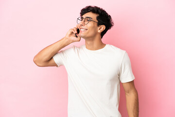 Young Argentinian man isolated on pink background keeping a conversation with the mobile phone