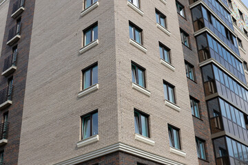 Corner of modern panel high-rise building with windows. Facing imitates a brick wall
