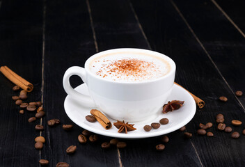 white cup with coffee latte sprinkled on top with chocolate or cocoa on a dark or black wooden background