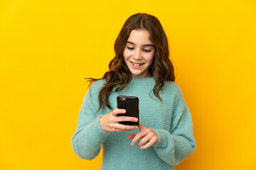 Little caucasian girl isolated on yellow background sending a message or email with the mobile