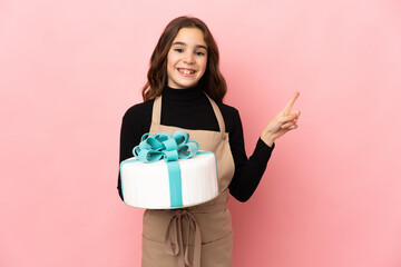 Little Pastry chef holding a big cake isolated on pink background pointing to the side to present a product