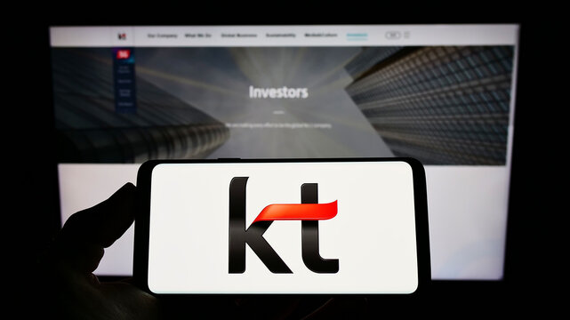 Stuttgart, Germany - 02-11-2022: Person holding mobile phone with logo of telecommunications company KT Corporation on screen in front of business webpage. Focus on phone display.