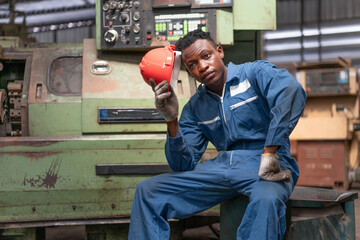 African American male engineer worker in safety vest with red helmet sitting on the old machine...
