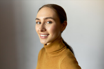 Close-up portrait of young smiling Caucasian female in turtleneck and long ponytail isolated over...