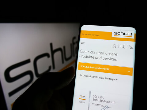 Stuttgart, Germany - 02-13-2022: Person holding smartphone with weboage of German credit protection company Schufa Holding AG on screen with logo. Focus on center of phone display.