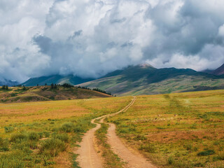 Way to the distance, way over the hill to the sky. Dirt road through the field. Atmospheric foggy mountain scenery with length road among hills.