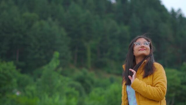 Portrait of young Indian woman standing in background of pine forest at Manali, Himachal Pradesh, India. Female enjoying nature in background of green trees during summer in Manali