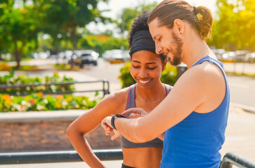Fototapeta premium couple of afro dominican girl and european white boy looking at the clock to start the exercise in the park, multiethnic couple