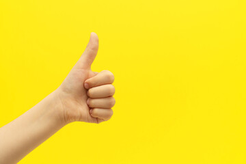 Child hand with satisfacting thumb up gesture on vivid yellow background.