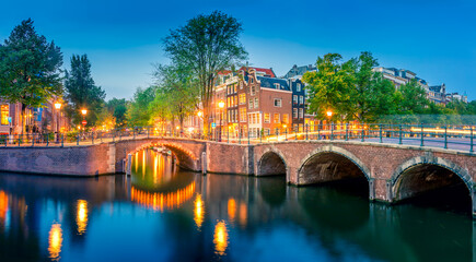 Fototapeta premium Romantic Amsterdam lit the lights. Evening panoramic view of the famous historic center with lantern lights, bridges, canals and cute Dutch houses.
