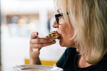 Fototapeta premium Blonde mature woman drinking coffee with donut in a cafe on summer terrace 