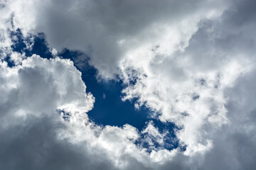 Fragment of a bright blue sky showing through gray fluffy clouds, for use as an abstract background and textures.