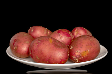 Several unpeeled pink potatoes on a white ceramic plate, close-up, isolated on a black background.