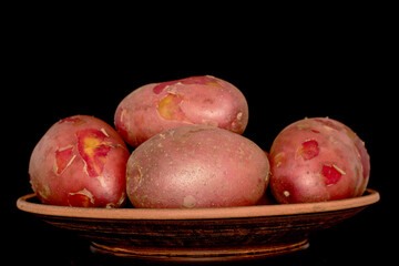 Several unpeeled pink potatoes on a clay plate, close-up, isolated on a black background.